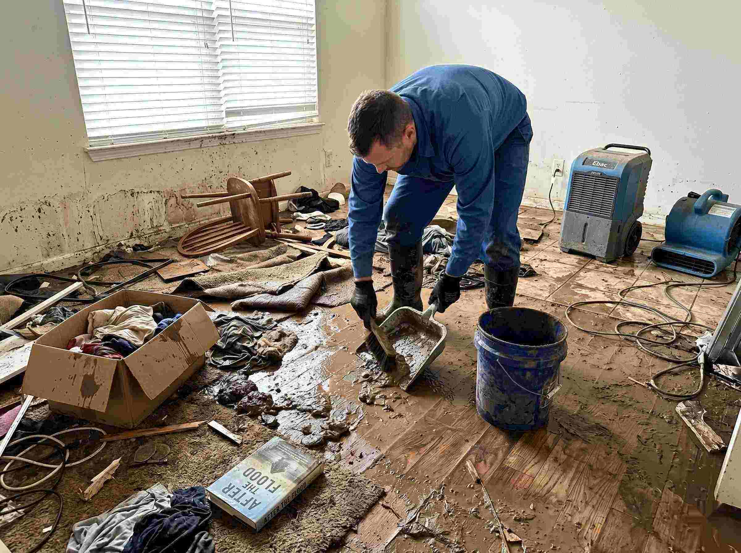 Realistic photo of a technician performing mud and debris removal after a home flood in Cape Coral, showing soaked furniture, wet flooring, and scattered debris during post-flood cleanup.